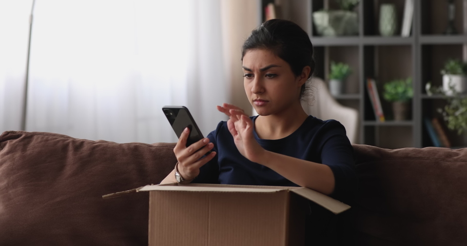 Unhappy young indian ethnicity woman unpacking carton box, feeling dissatisfied with getting wrong or damaged order, writing negative feedback in mobile application, internet shopping concept. Royalty-Free Stock Footage #1068157058