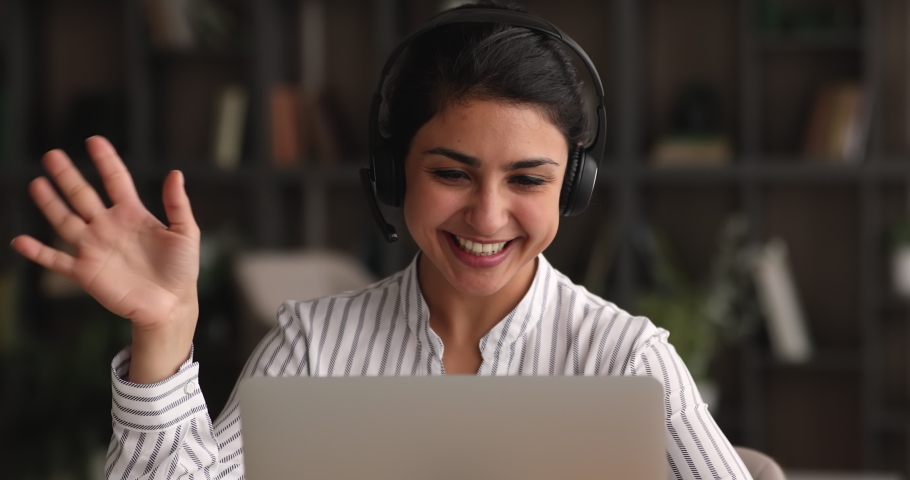 Friendly smiling millennial indian businesswoman in wireless headphones with microphone waving hand making hello gesture, starting online meeting web camera video call conversation with colleagues. Royalty-Free Stock Footage #1068157502