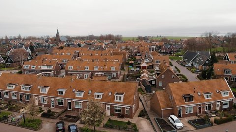 Aerial flying near the typical Dutch houses of Volendam showing the typical lines of homes and street this harbor town is popular tourist attraction in Netherlands blue sky background and clouds