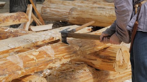 Man lumberjack cutting large log with axe - wood shavings, chips flying at summer historical medival festival - close up, slow motion. Craftsmanship, revival, reenactment, handwork concept