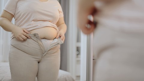 Oversize woman zipping up trousers, excess belly fat, unhealthy lifestyle, diet