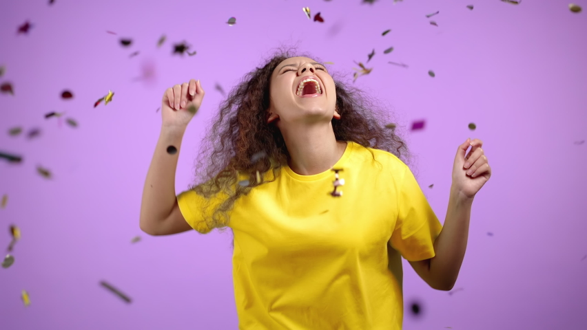 Happy woman dancing, having fun, screaming WOW, rejoices over confetti rain in violet studio. Champion girl. Concept of celebrating, party, winning | Shutterstock HD Video #1068168440
