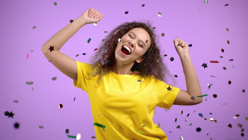 Happy woman dancing, having fun, screaming WOW, rejoices over confetti rain in violet studio. Champion girl. Concept of celebrating, party, winning Royalty-Free Stock Footage #1068168440