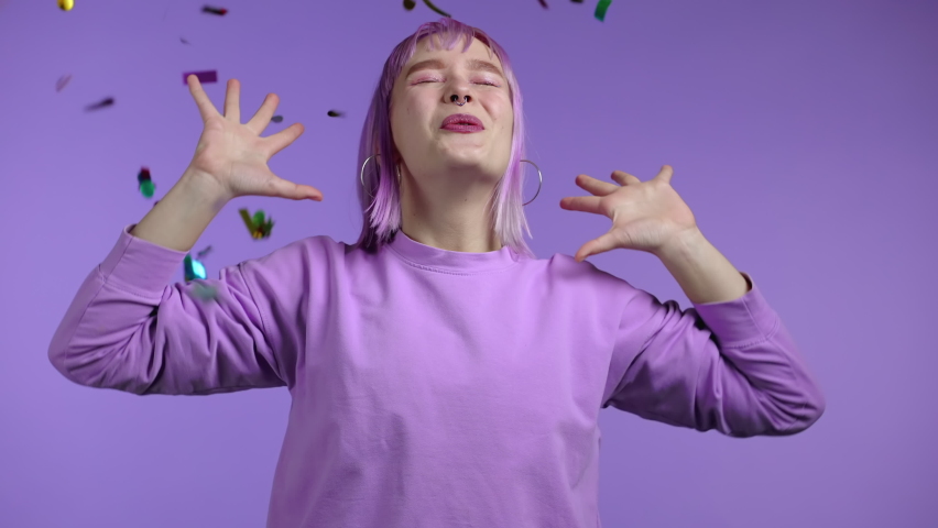 Excited unique woman clapping hands, having fun, screaming WOW, rejoices over confetti rain in studio. Extraordinary girl with violet dyed hairstyle. Concept of celebrating, party, winning Royalty-Free Stock Footage #1068168452