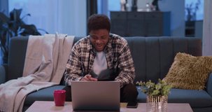 Young african cheerful man using laptop for distant communication relationships calling best friends or family sharing positive news staying home studying.