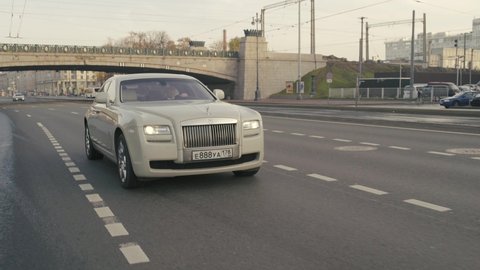 Saint-Petersburg, Russia — October, 2020: A white Rolls-Royce Phantom starts and drives quickly along the city street at sunrise on an autumn day.