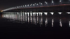 Beautiful shiny reflection of bright lanterns with cold light in the big Dnieper river under a long bridge passing over it. HD realtime video