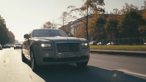 Saint-Petersburg, Russia — October, 2020: A prestigious white Rolls-Royce car is driving around the city. The camera moves away from the close-up of the wheel to a wide view of the car.