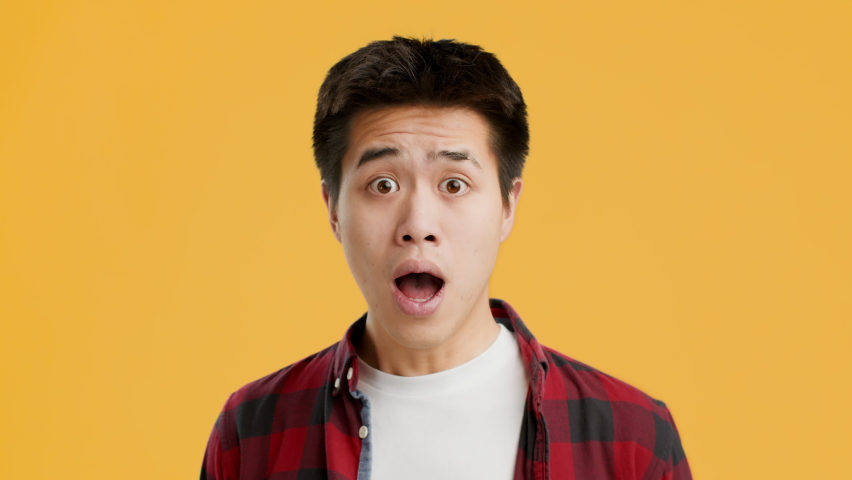 Shocked Asian Guy Looking At Camera In Surprise Posing With Open Mouth And Bewildered Eyes, Relieving After Shock Over Yellow Studio Background. Portrait Of Surprised Emotional Chinese Man Concept Royalty-Free Stock Footage #1068184595