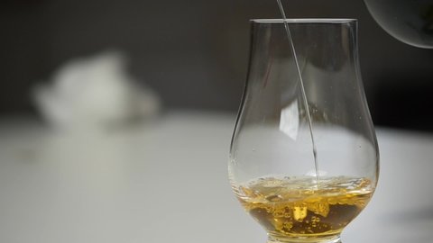 Taking a bottle of alcoholic and spiritous drink and pouring it in a whiskey glass in slow motion. The liquid with small bubbles swings elegantly on a bottom of the glass.