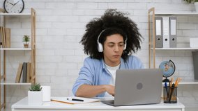 Bushy-Haired Black Guy Wearing Headphones Listening To Music At Laptop Sitting At Desk At Home. Modern Youth Lifestyle. Online Podcast And E-Learning. Remote Education Concept
