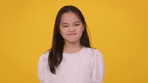 Bad idea. Little asian girl shaking her head in denial and frowing her face, orange studio background, slow motion