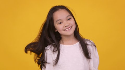Little model. Cute cheerful asian girl shaking her hair and smiling at camera, orange studio background