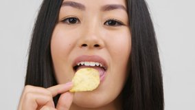 Chinese Woman Eating Crispy Potatoes Chips Enjoying Unhealthy Snack Standing On White Studio Background, Closeup Portrait. Junk Food, Bad Nutrition Habit Concept - Powered by Shutterstock - Get 15% off with code: PIKWIZARD15