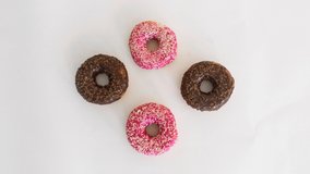 Chocolate and strawberry Donuts stop motion overhead, flat lay on white background. Four donuts spinning, one donut eaten. Time lapse. Donut dance