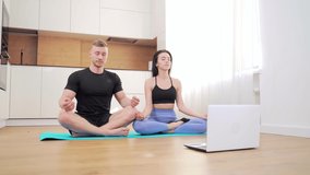 Happy young married couple performing exercises online at home in front of laptop. A sports family team practicing yoga together on a mat in the lotus position. relaxation and meditation in apartment