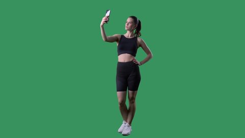 Healthy fitness young woman taking selfie photos with cell phone. Full body length on green screen chroma key. 