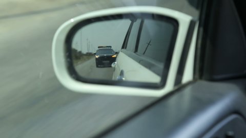 Yerevan, Armenia - May 2018 - Police car in the side mirror chasing a car on highway. Police chase, the car is running away from the chase