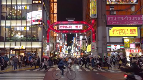 tokyo, japan - october 25 2019: Tilt-up video of traffic in front of the pedestrian crossing and the neon-lit arch of the kabukicho ichibangai street in Shinjuku illuminated at night by signs.
