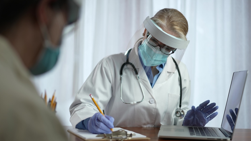 Woman doctor wearing face shield face mask and surgical gloves looks at X-ray image of patient. Concept of doctor with PPE personal healthcare in office. | Shutterstock HD Video #1068209492