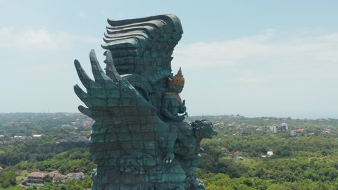 Side dolly aerial view of giant Garuda Wisnu Kencana statue in Bali, Indonesia. Statue of Garuda being ridden by Vishnu rising above the town