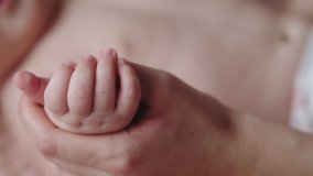 Close-up, mom is holding her newborn baby's tiny hand, love in touch. Mom and her child. Happy family concept. Parenthood. Motherhood. Slow motion 4K video