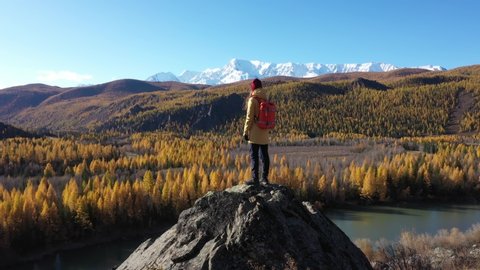 Backpacker in Golden Autumn in Altai Mountains, Siberia, Russia. Camera Flying Over the Traveler with Beautiful Autumn Mountains on Background