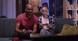 African american happy young adult couple dating on evening spending time playing computer games on console josticks together.
