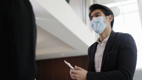 Asian businessman connect with travel Receptionist in airport lounge. Telephone operator to check hotel room Reserve. Mask and face shield to prevent COVID-19 infection. Concept Service business