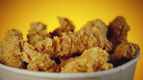 Bucket of crispy golden chicken wings, legs and strips. Side view over orange background