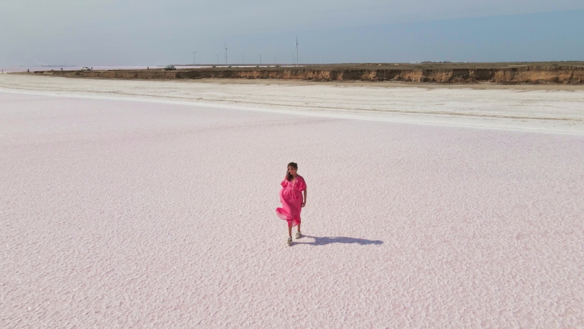 Aerial drone shot of beautiful joyful woman in pink dress jogging and running across Salt Flats flats of Sivash pink lake, Ukraine