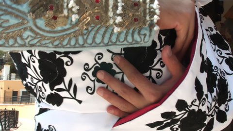Close-up of male bullfighter hands folding white and black cape. Classic matador wearing blue suit of lights and white cape with black flowers print. Traditional bullfighting