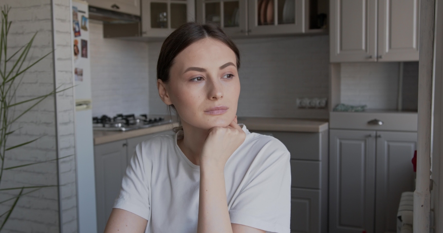 Portrait of pretty young woman with brown hair sitting at kitchen table. Smiling brunette in casual outfit enjoying free time at home. 