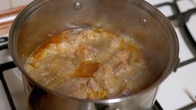 Simmering Pieces of Pork Meat in Saucepan on Gas Stove in Tomato Sauce. Home kitchen. Cooking juicy stewed pork on dinner. Boiling process, evaporation of water. Concept of food. Zoom. Close-up.