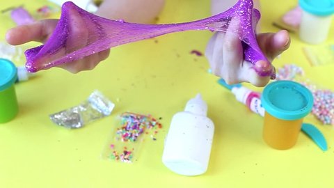 Making slime at home. child holding and stretching colorful slime. DIY concept.Kids hands make purple slime with sequins on a yellow background. Flat lay, top view.
