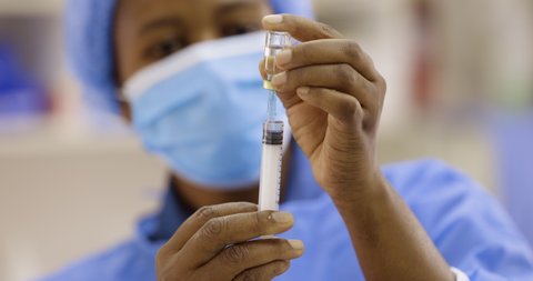 Black African female doctor nurse pulling Covid-19 vaccine liquid from vial