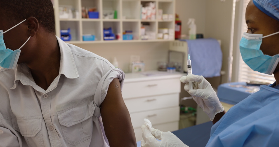 Black African female doctor nurse gives a Black African male patient the Covid-19 vaccine injection | Shutterstock HD Video #1068260612