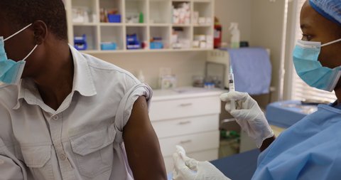 Black African female doctor nurse gives a Black African male patient the Covid-19 vaccine injection