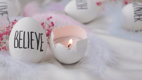 Footage of igniting a candle in Easter eggs Composition. Words drawn with pen. Believe. Cozy home interior decor, burning candles hygge, decoration and easter concept - candles burning