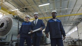  Low angle tracking shot with slowmo of male and female workers in uniforms and hard hats walking through plant facility and listening to male manufacturing engineer with blueprint give instructions - Powered by Shutterstock - Get 15% off with code: PIKWIZARD15