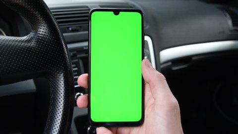 Man holding mobile phone, smartphoneon the background of a black car interior. Green screen, blank phone, application.Swipe to the right with your thumb. Close up