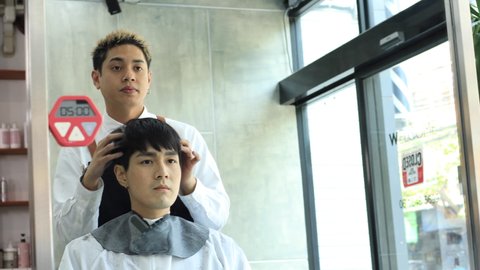 Professional asian hairdresser trimming, cutting man's hair with scissors and checking hair design in modern salon.  Beauty salon business concept.