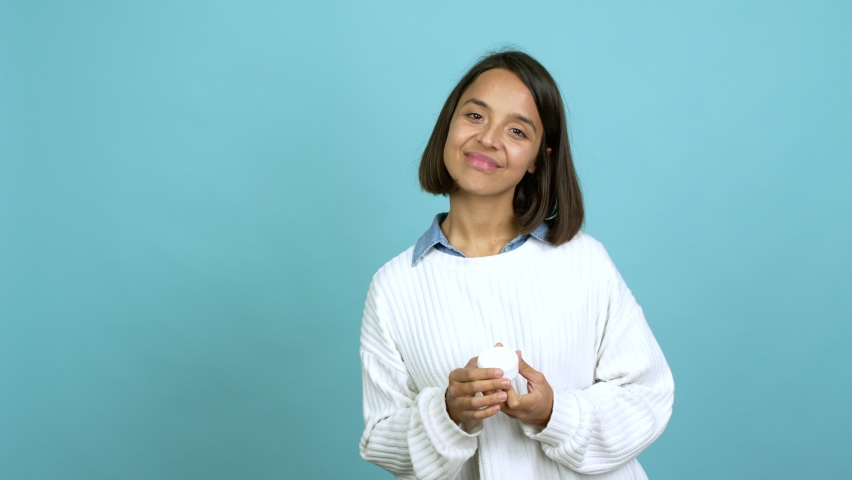 Young brunette woman with moisturizer over isolated background