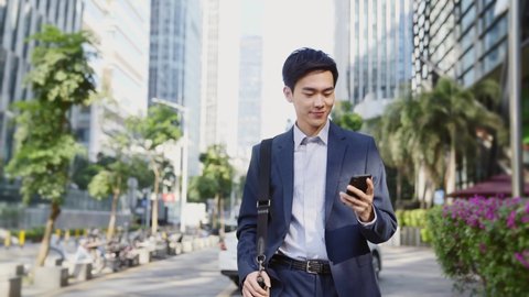 young asian business man looking at cellphone while walking on street in modern city