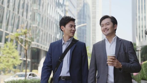 two asian business men walking talking on street in modern city