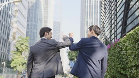 rear view of two asian businessmen talking while walking on street in modern city