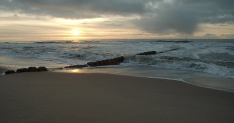 Waves breaking on the groynes on the island Sylt with the sunset in the background