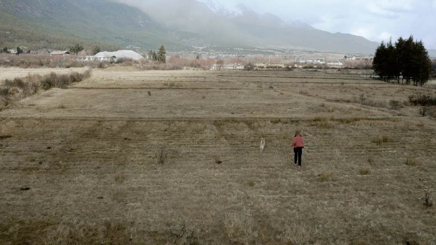 Free woman and dog running through remote grass field, Chinese mountains, aerial