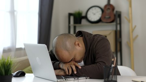 Tired businessman working with laptop. He covered his mouth with his hand and yawned. He is very sleepy and take off glasses. He work from home.
