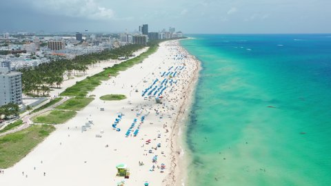 Incredible white sandy beach at the transparent green blue ocean. Happy people enjoying summer vacation in beach resort. Amazing vibrant teal color sea waters. Aerial view Miami beach tropical nature
